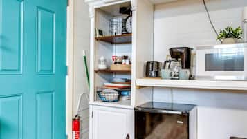A kitchen with a teal door, a microwave, a coffee maker, and a small refrigerator.
