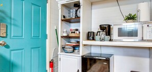 Una cocina con una puerta color turquesa, microondas, cafetera y refrigerador pequeño.