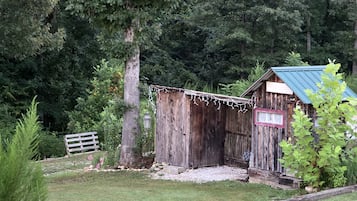 A rustic wooden barn with a metal roof, surrounded by a grassy area and trees.