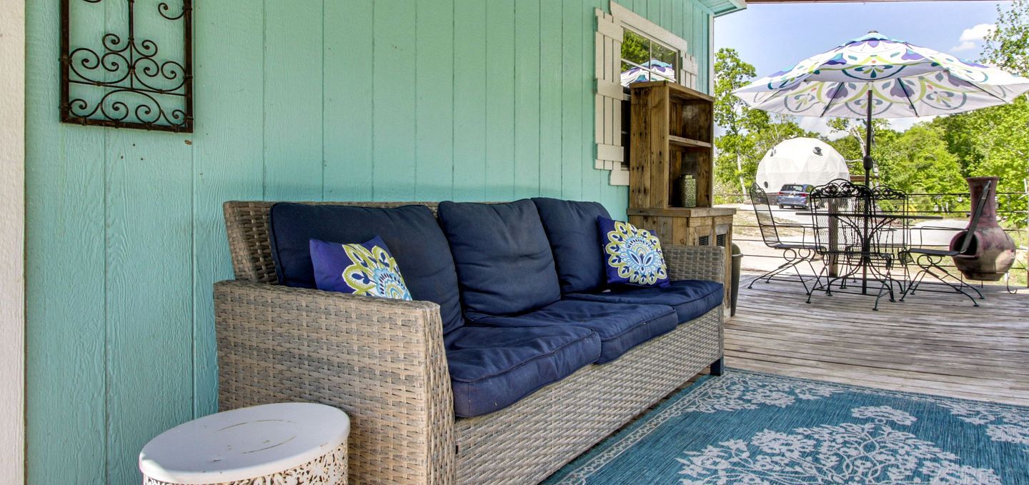 A wicker sofa with cushions, a small round table, and a patterned rug on a wooden deck.