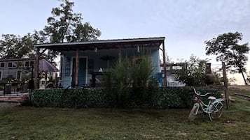 A small building with a porch, surrounded by a grassy area and trees.