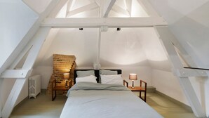 Une chambre avec un plafond en pente, un lit, une table de chevet, une lampe et un mur en briques.