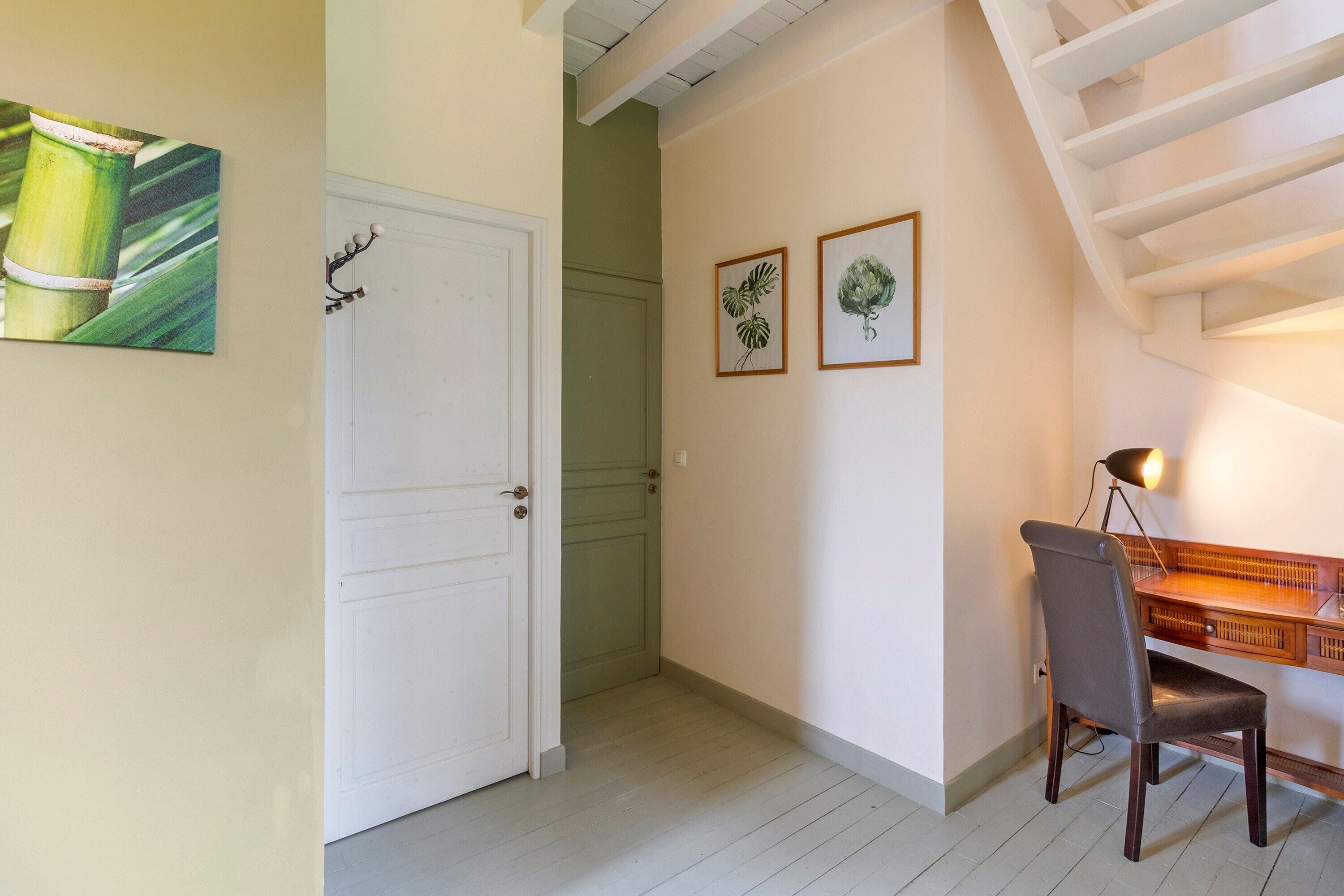 Un couloir avec une porte blanche, un bureau avec une chaise et deux reproductions botaniques encadrées accrochées au mur.