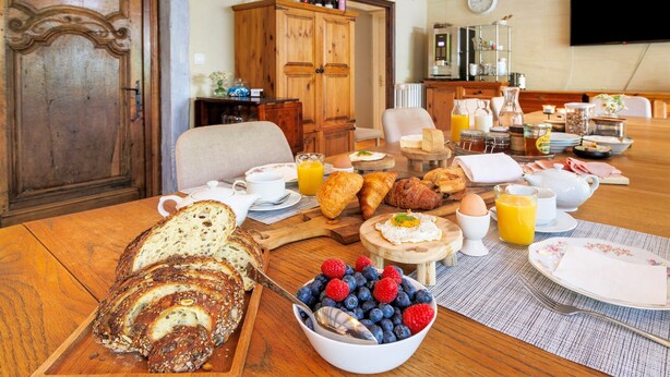 Une table en bois dressée pour le petit-déjeuner, avec du pain, des viennoiseries, des fruits et des boissons.