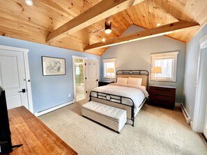 A bedroom with a bed, bench, wooden ceiling beams, and a door.