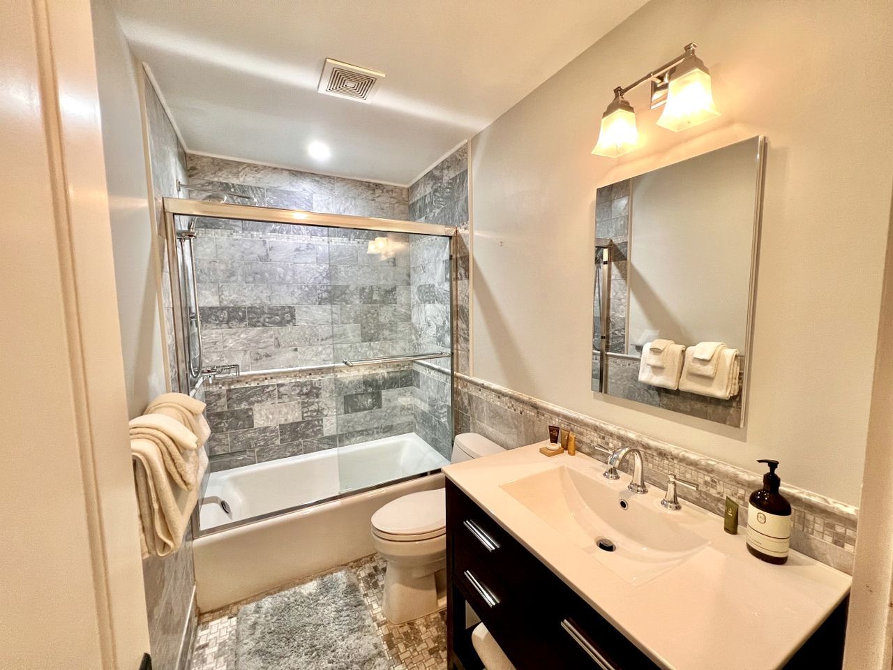 A bathroom with a glass-enclosed shower, a bathtub, a toilet, and a vanity with a sink and mirror.