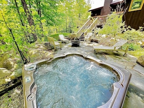 A hot tub surrounded by outdoor furniture, a wooden staircase, and a building with a porch. - Mountain Retreat with Outdoor Living Space and Ping Pong Table in Vermont (Winhall)