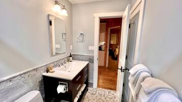 Une salle de bain avec des toilettes blanches, un lavabo avec un miroir, un porte-serviettes et un sol carrelé.