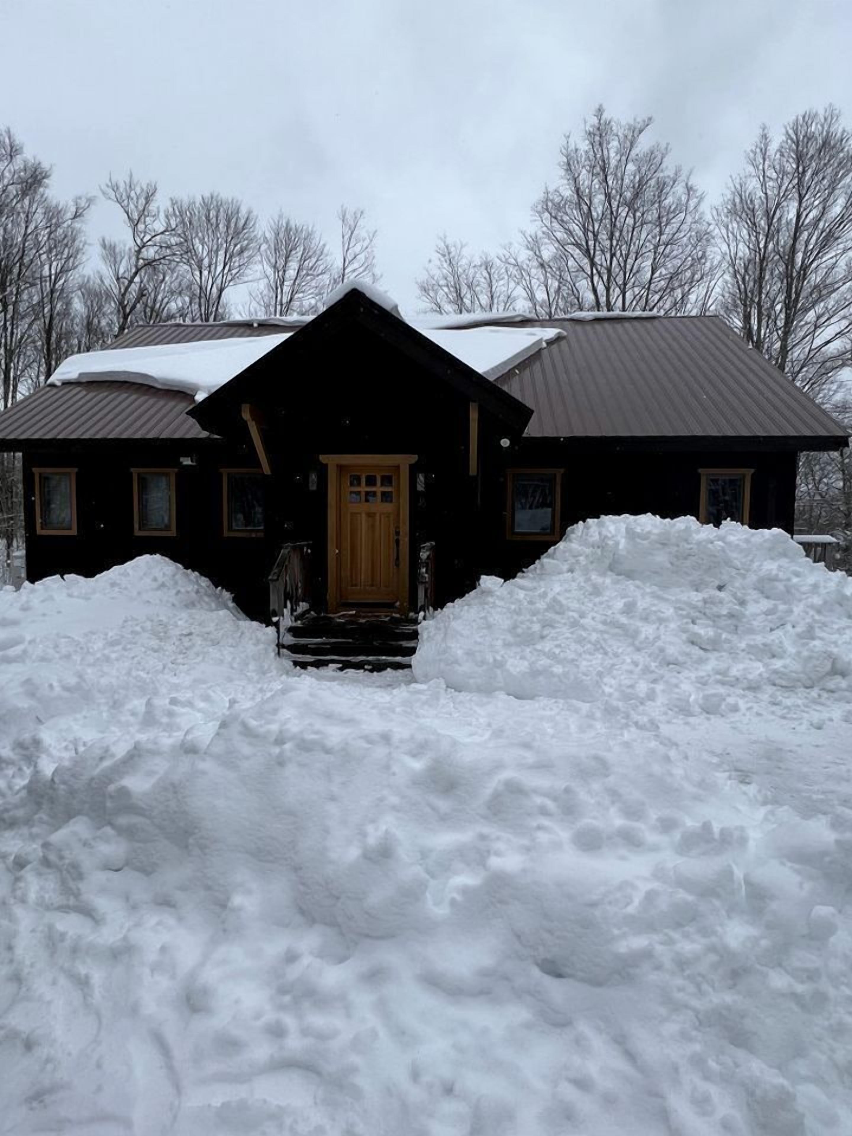 Una cabaña de troncos con puerta y ventanas de madera, rodeada de nieve.