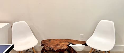 Una habitación con una mesa de centro de madera, dos sillas blancas y piso alfombrado.