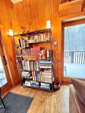 A wooden interior with a bookshelf, a door leading outside, and a view of a snowy landscape.