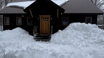 A log cabin with a wooden door and windows, surrounded by snow.