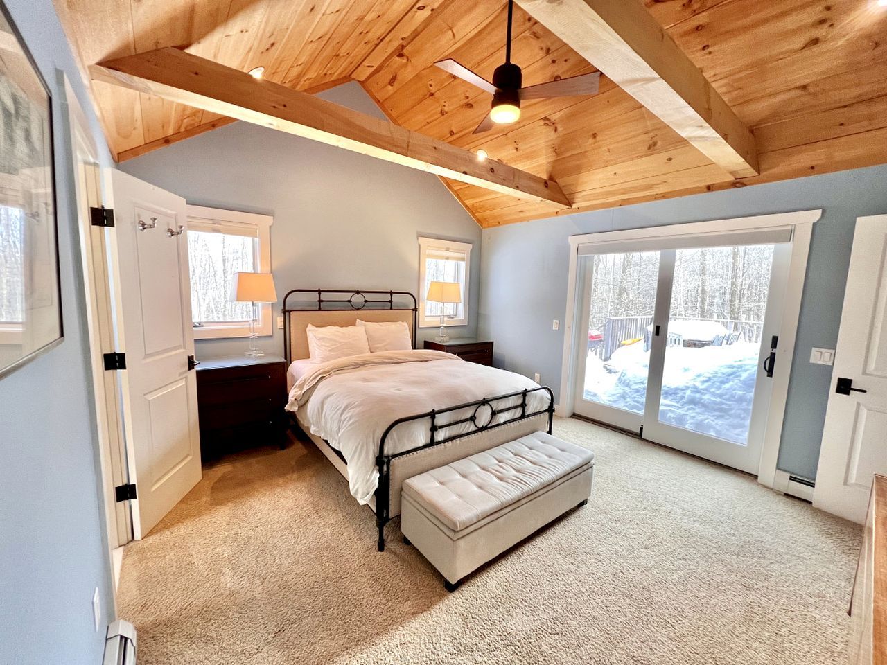 A bedroom with a bed, bench, and large windows.