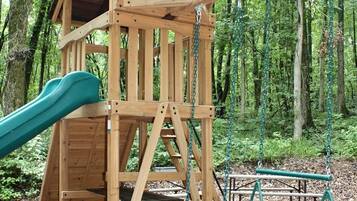 A wooden play structure with a slide and swings in a wooded area.