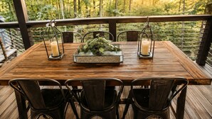 A wooden deck with a table set for four, surrounded by metal chairs, with a railing and forest view in the background. - Incredible Secluded Cabin wit Barbecue and Privileged Sights in Tracy City, Tennessee (Tracy City)