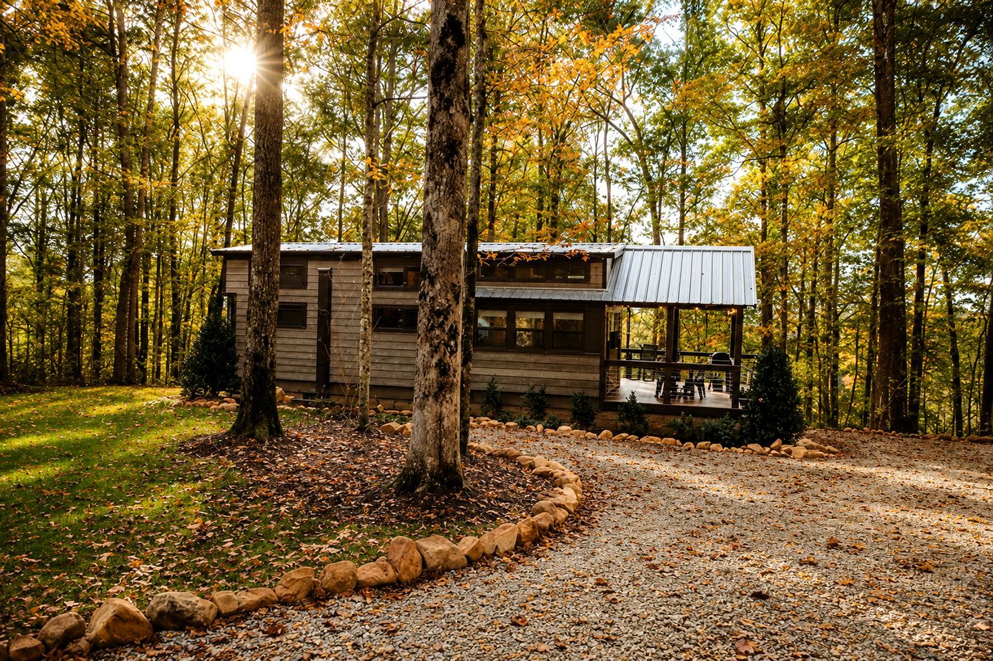 A cabin with a porch, surrounded by trees and a gravel path.