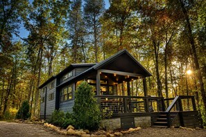 Une cabane dotée d’une véranda, entourée d’arbres.