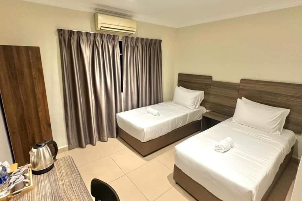 Habitación de hotel con dos camas, cabecero de madera, escritorio con tetera y cortina.