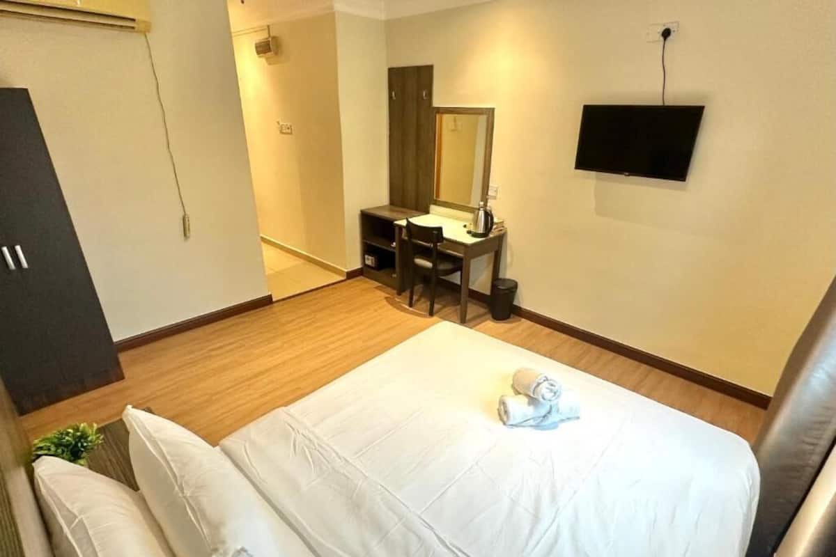 Una habitación de hotel con una cama, un escritorio con silla, un televisor y un armario.