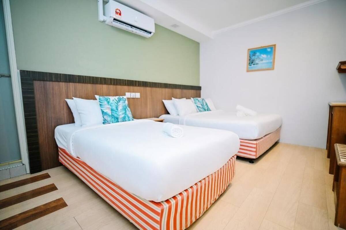 A hotel room with two beds, striped bedding, a wooden headboard, a small picture on the wall, and an air conditioning unit.
