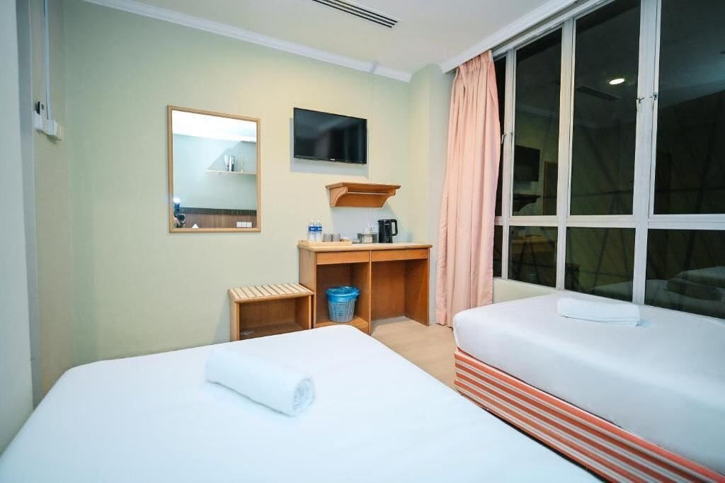 Una habitación de hotel con cama, escritorio con espejo, televisión y ventana con cortinas.