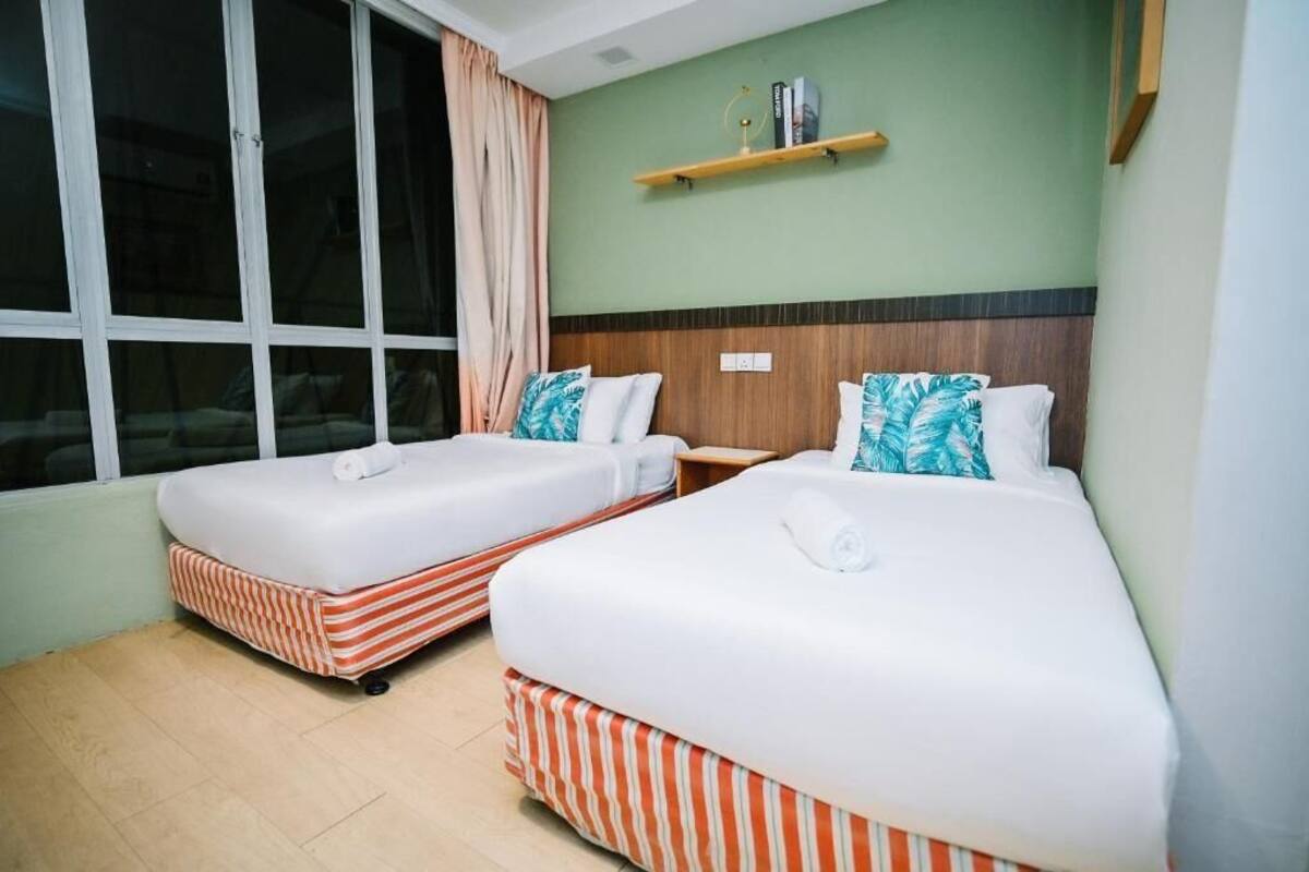 A hotel room with two beds, a window with curtains, a shelf with books, and a wooden headboard.