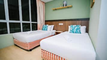 A hotel room with two beds, a window with curtains, a shelf with books, and a wooden headboard.