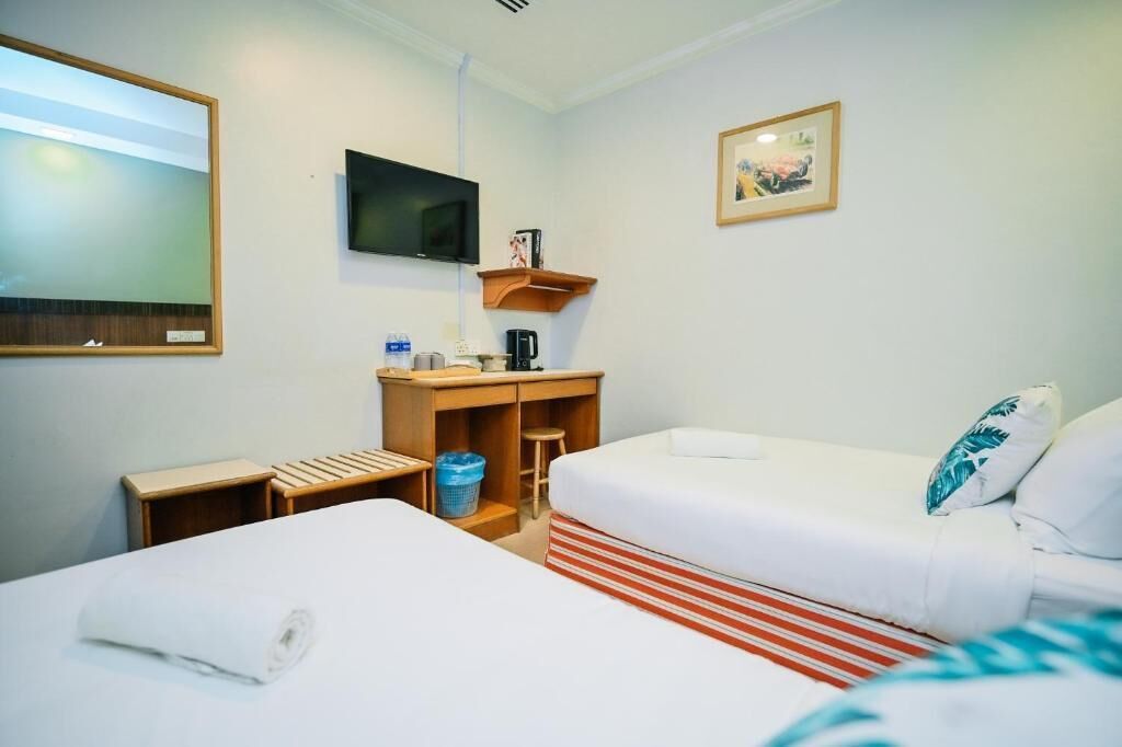 Habitación de hotel con dos camas, televisor, escritorio pequeño y una estantería con un cuadro.
