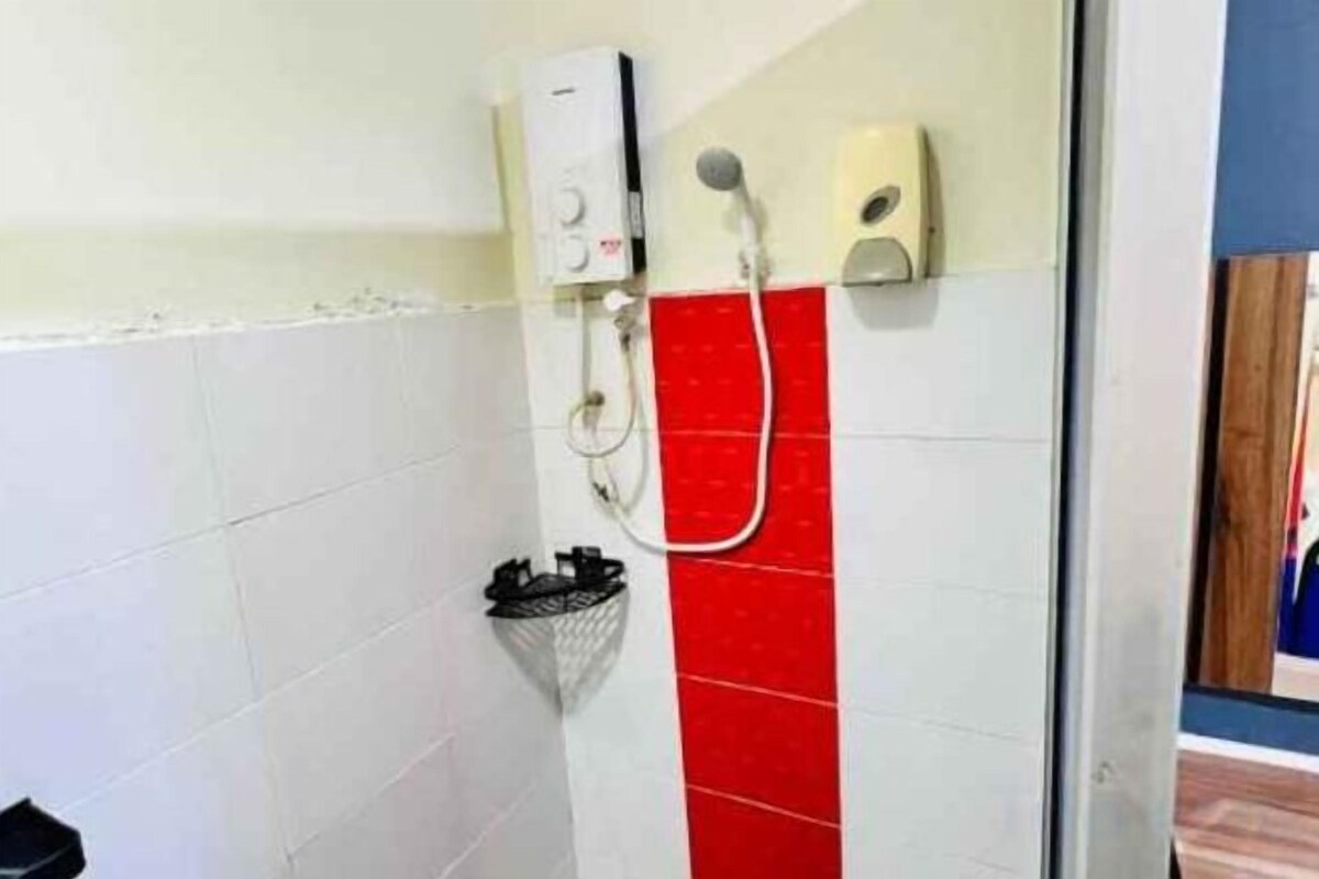 A shower area with a white wall, a red tiled section, a handheld showerhead, and a wall-mounted control panel.