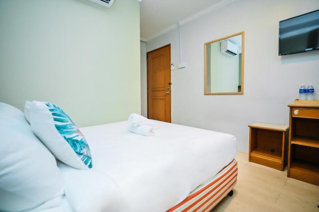 Una habitación de hotel con una cama, una mesita de noche de madera, un televisor y un espejo en la pared.