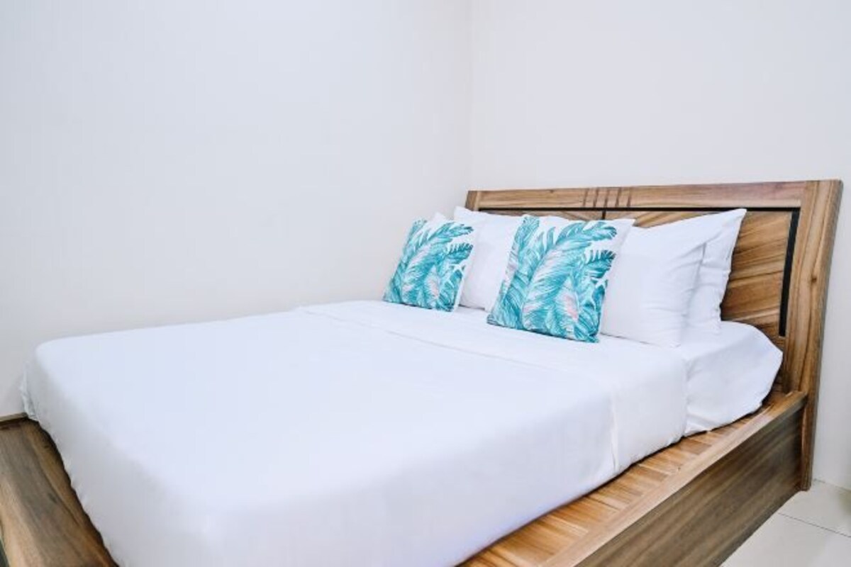 A bed with white bedding and two pillows with a leaf pattern.