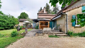 A house with a gravel driveway, a patio with outdoor furniture, and a covered area with a bar. - Guest Room "Chambre du Parc" (Thiviers)