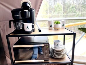 A kitchen area with a Keurig coffee maker, a microwave, and a stack of plates on a table. - Spacious Dome with Lofted Interior and Furnished Deck in Kentucky (Cadiz)