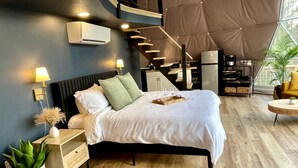 Un dormitorio moderno con cama, mesitas de noche, una planta pequeña y una escalera que lleva a un nivel superior.