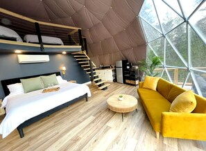 Um interior moderno com uma cama, sofá e mesa de centro redonda, uma escada e uma janela grande.