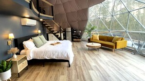 A modern bedroom with a bed, bedside tables, a sofa, and a round coffee table. - Spacious Dome with Lofted Interior and Furnished Deck in Kentucky (Cadiz)