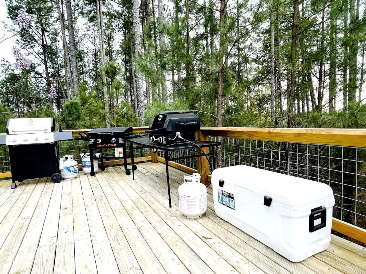 A deck with a grill, a cooler, and propane tanks.