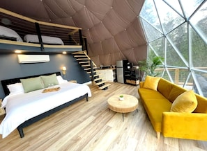 A modern interior with a bed, sofa, and round coffee table, a staircase, and a large window.