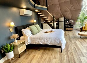 A modern bedroom with a bed, bedside tables, a small plant, and a staircase leading to an upper level. - Spacious Dome with Lofted Interior and Furnished Deck in Kentucky (Cadiz)