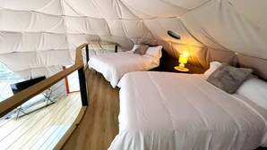 A tent-style room with two beds, a wooden deck, and a small table with a lamp. - Spacious Dome with Lofted Interior and Furnished Deck in Kentucky (Cadiz)