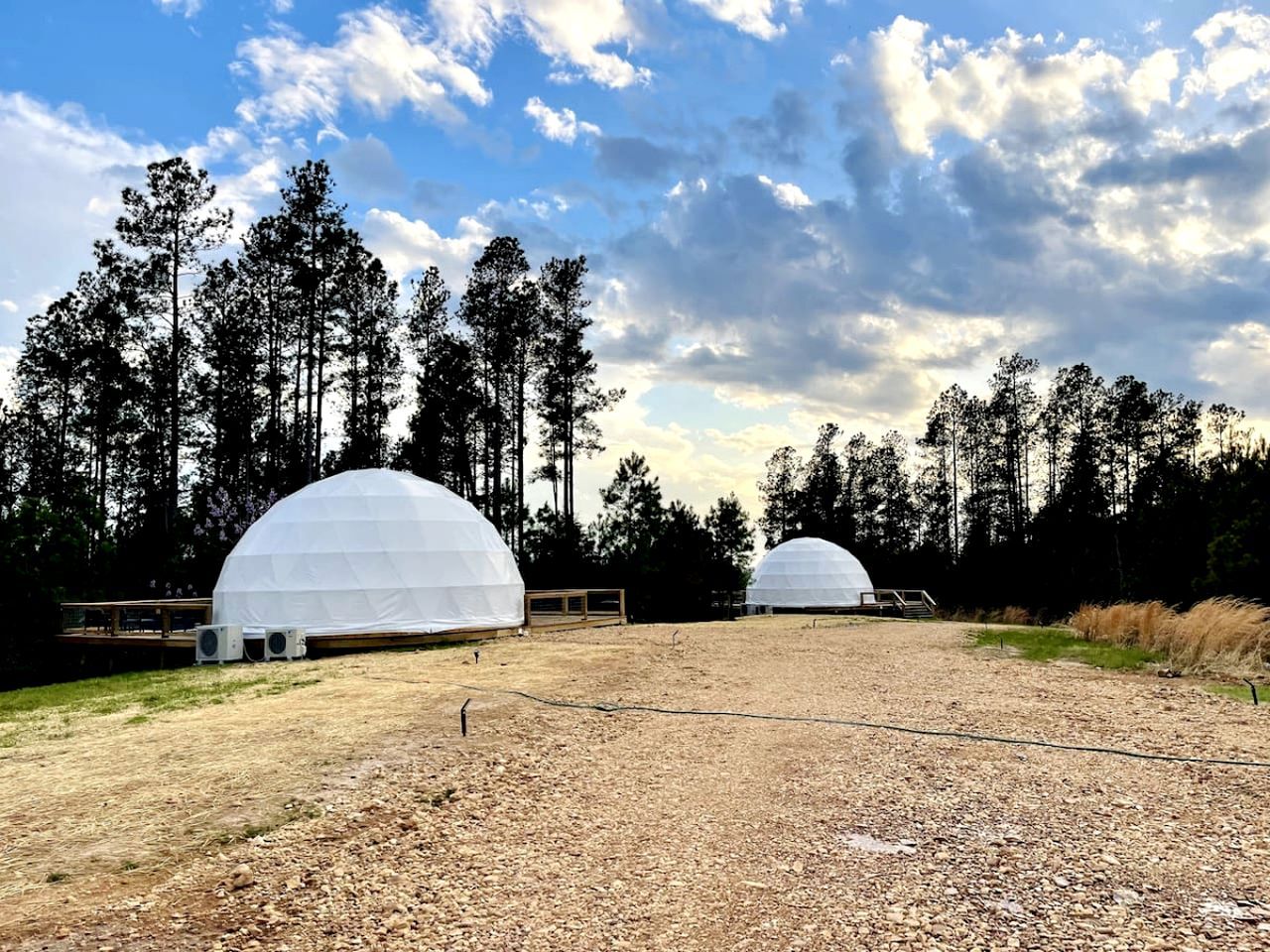 Two dome-shaped structures in an open field with a forest in the background.