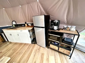 A compact kitchen with a refrigerator, coffee maker, and storage shelves.