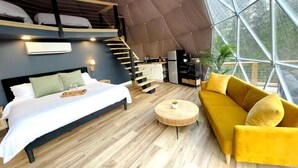 Un interior moderno con cama, sofá y una mesa de centro redonda, una escalera y un gran ventanal.
