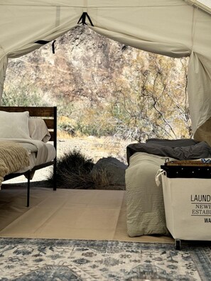 A tented room with a bed, a small table, and a bag labeled 'LAUNDRY NEW ESTABLISHMENT.' - Remote Expansive Tented Cabin Incredible for a Glamping Experience in Nevada (Boulder City)