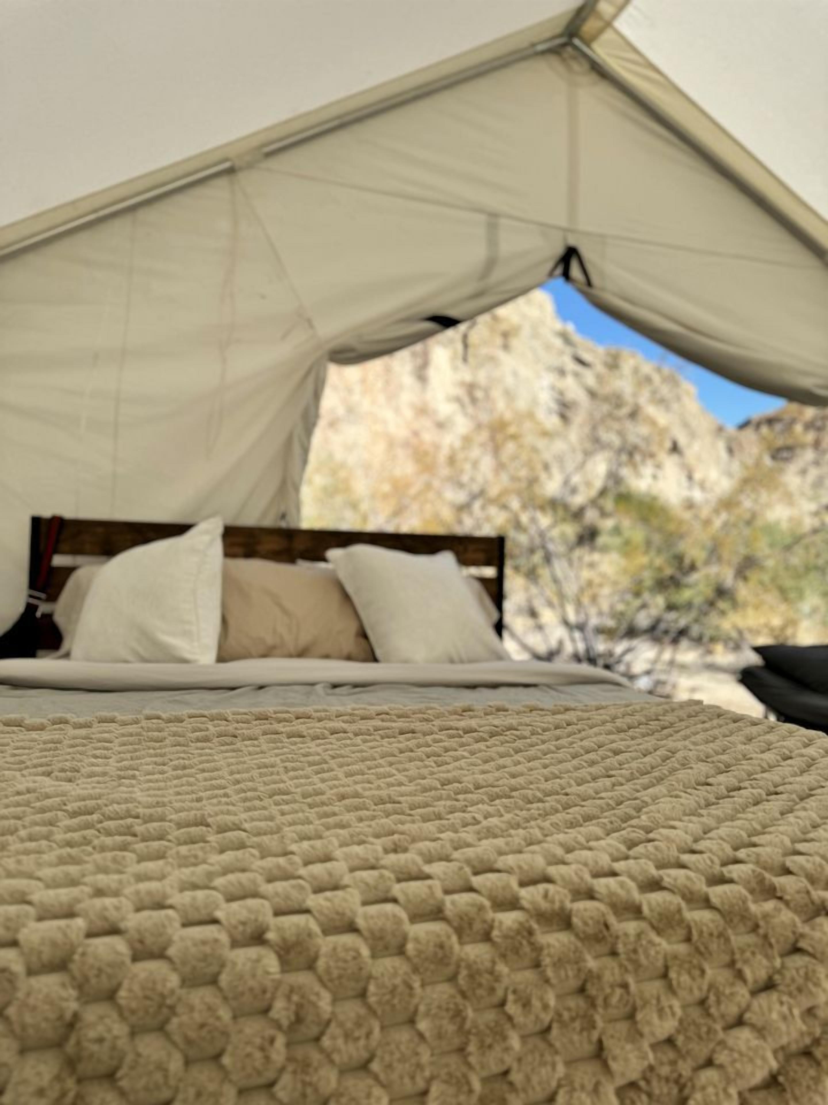 A bed with a textured blanket, a canopy, and pillows, set against a natural backdrop.