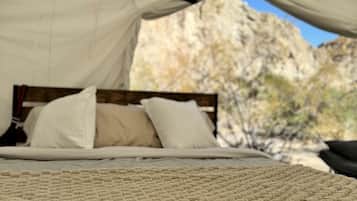A bed with a textured blanket, a canopy, and pillows, set against a natural backdrop.