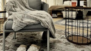 A tented room with a grey chair, a small table with a lamp, and a pair of slippers on the floor.