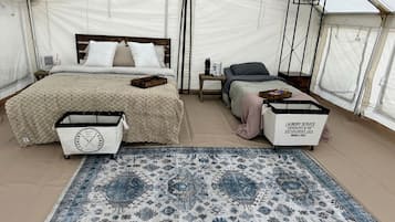 A tented accommodation with a bed, a small table, a chair, a rug, and a laundry service cart.