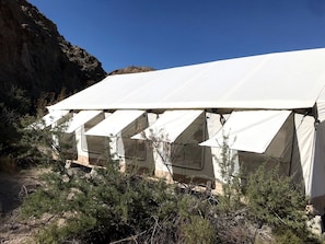 A row of white tents with a rocky cliff in the background.