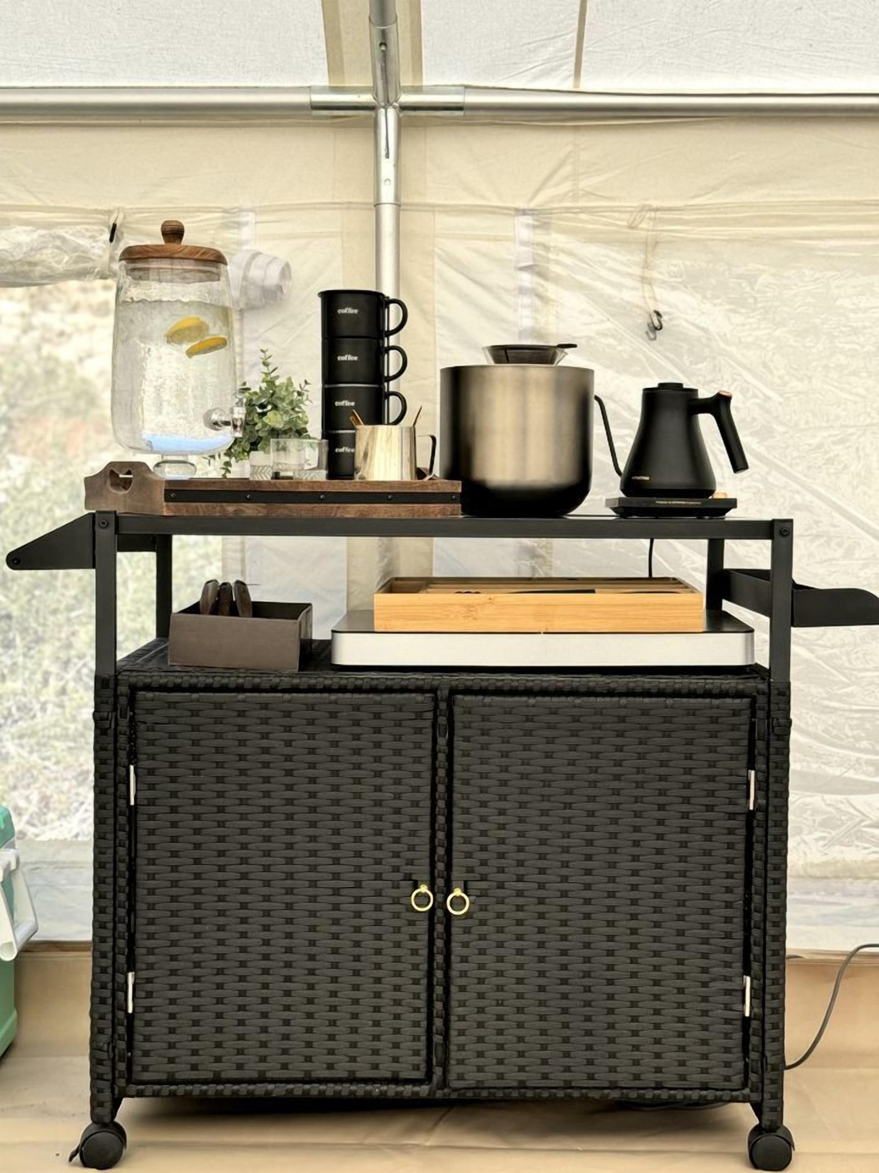 A black wicker cart with a metal frame, a glass jar with a lid, a black coffee maker, a stainless steel pot, and a black kettle.
